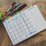 A planner laid out on a desk with colorful tabs and pens and highlighters above.